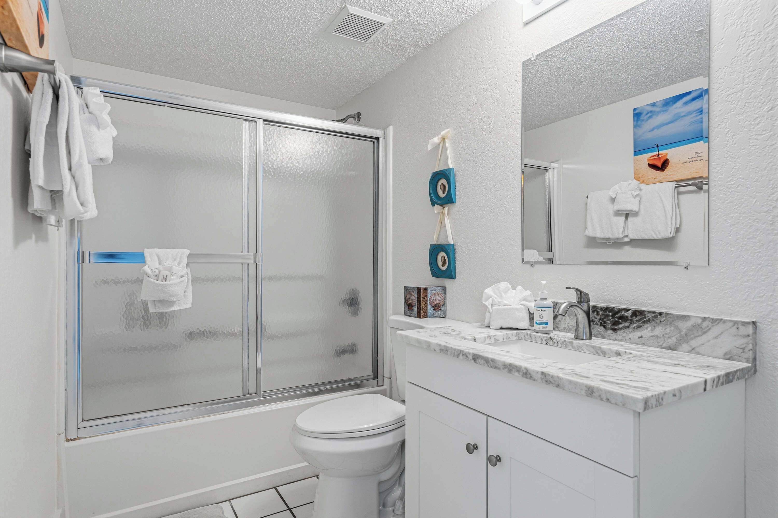 A bathroom with a glass shower enclosure, a toilet, a sink with a marble countertop, and a mirror above the sink.