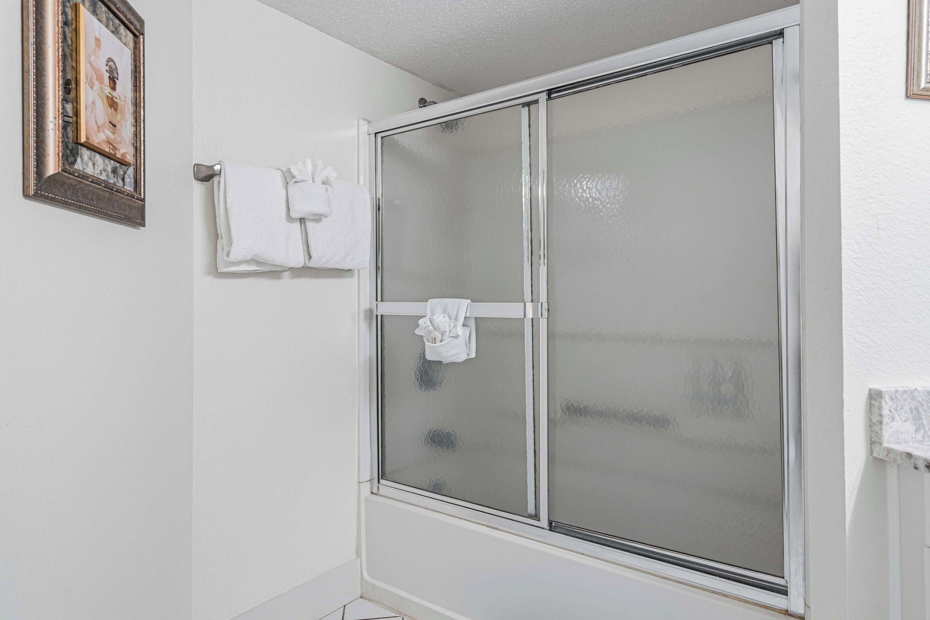Une salle de bain avec une porte de douche en verre dépoli, un porte-serviettes avec deux serviettes blanches et un tableau encadré au mur.