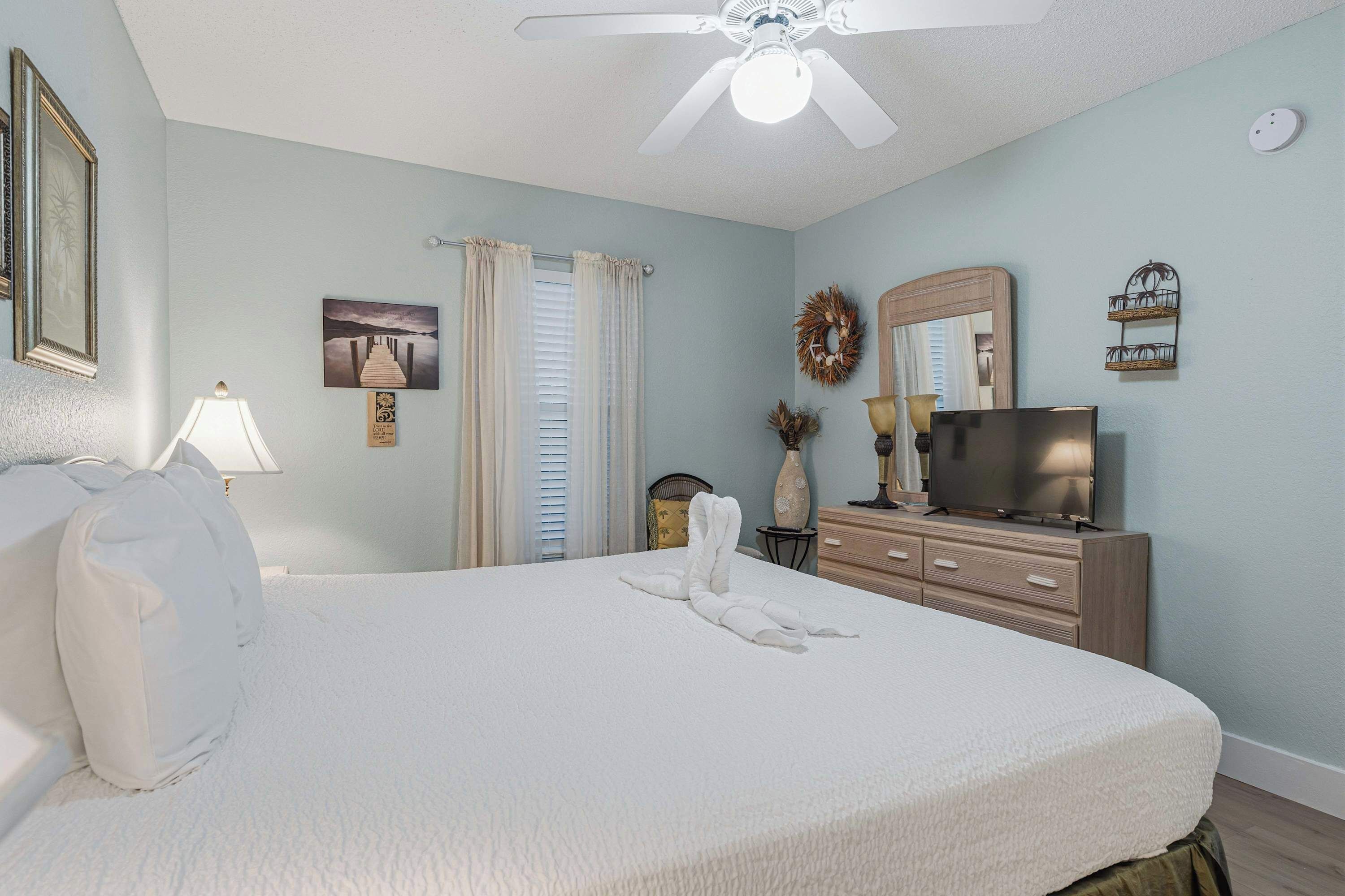 A bedroom with a bed, a ceiling fan, a TV, a dresser, and a mirror.