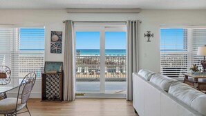 Une pièce avec vue sur la plage, une porte-fenêtre coulissante, un canapé blanc, une table à manger avec des chaises et un élément décoratif mural.