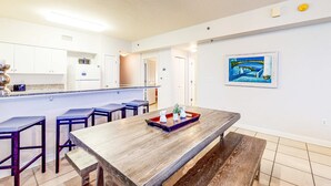 A modern kitchen with white cabinets, a wooden dining table, and a blue painting on the wall. - Gulf-front getaway with pools, hot tub & central AC (Panama City Beach)