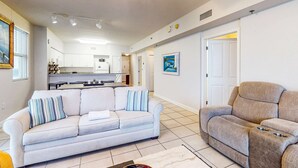 A living room with a sofa, a recliner, a dining table, and a kitchen in the background. - Gulf-front getaway with pools, hot tub & central AC (Panama City Beach)