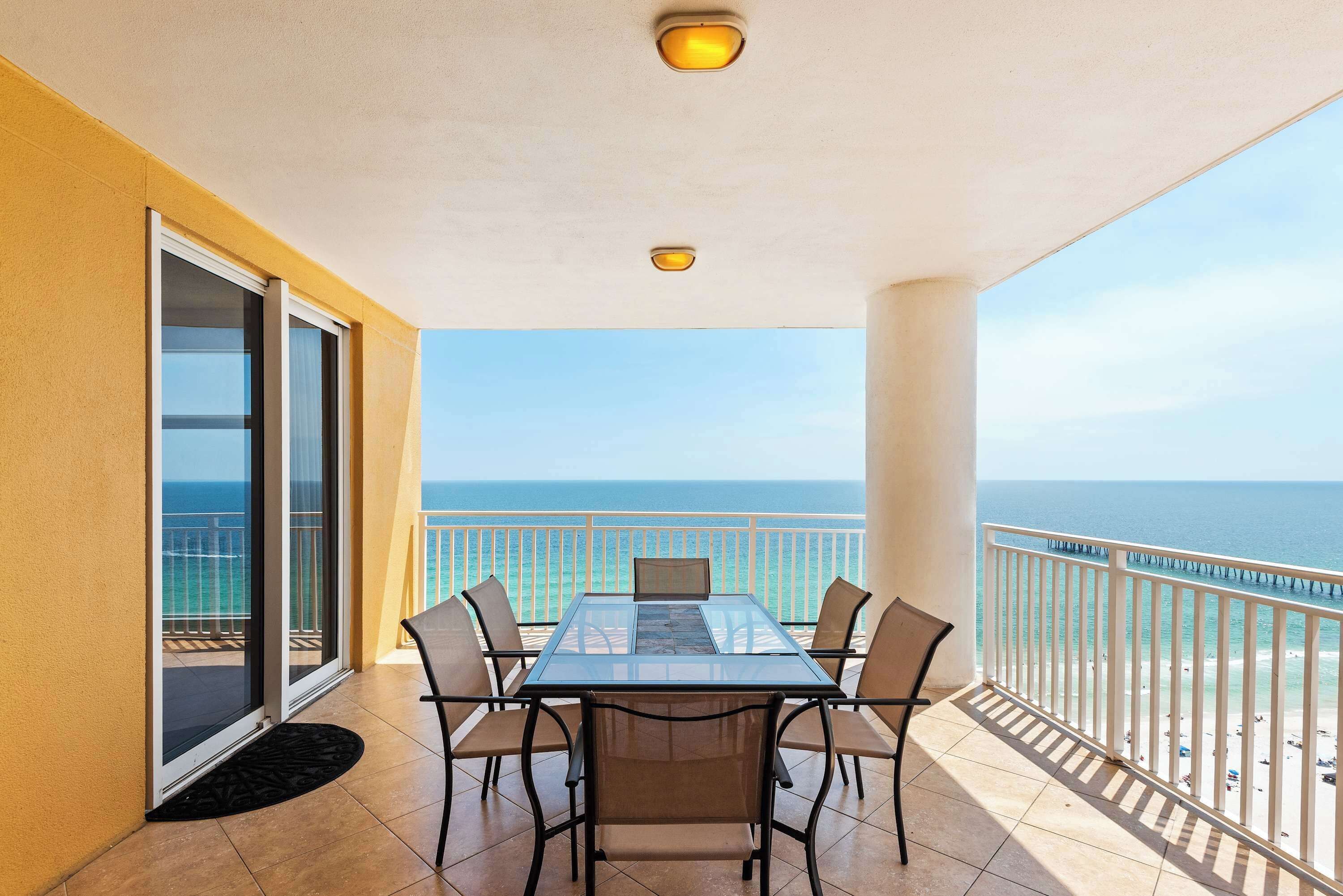 A balcony with a glass table and chairs, a view of the ocean, and a railing.