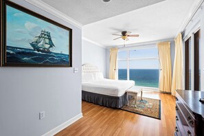 Ein Schlafzimmer mit einem Bett, einem Deckenventilator, einem großen Fenster mit Vorhängen und einem Gemälde eines Schiffes an der Wand.