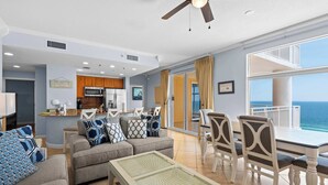 A spacious living area with a sofa, chairs, a dining table, and a balcony with a view of the ocean. - Beachfront resort condo with Gulf views, outdoor pool, & private balcony (Panama City Beach)