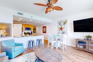 A modern living room with a blue sofa, a round wooden table, and a ceiling fan. - Gulf-view escape near the beach with pool, hot tub, balcony & w/d (Panama City Beach)