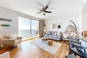 Ein geräumiges Wohnzimmer mit einem gro ßen Schiebeglastür, die auf einen Balkon führt, einem Deckenventilator, einem grauen Sofa, einem runden Couchtisch und einem Hängekorbsessel.