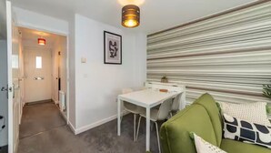 Un espacio habitable compacto con zona de comedor, sofá verde y pared a rayas.