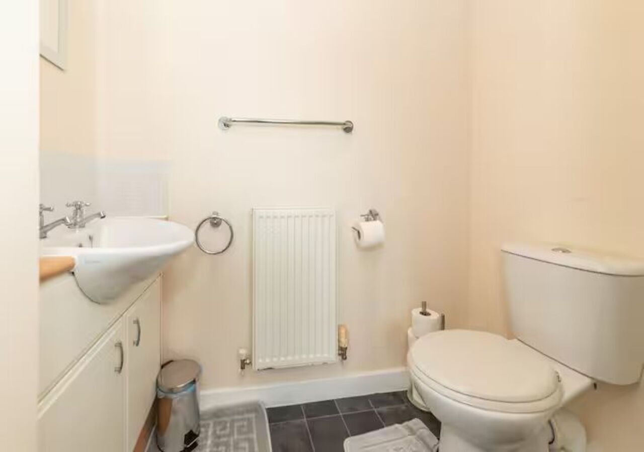 A bathroom with a white toilet, a sink, a radiator, and a handrail.