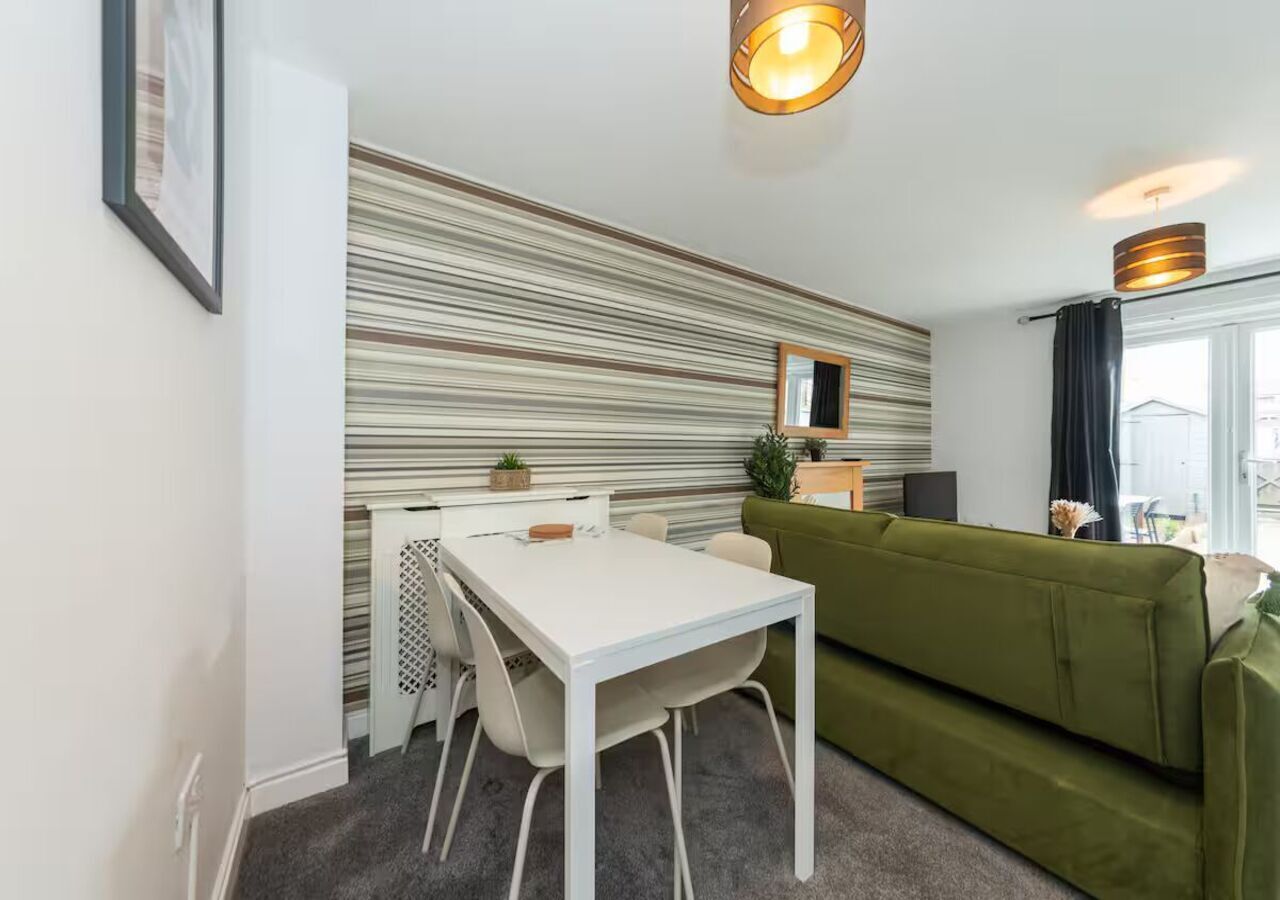 A compact living space with a striped wall, a white table, a green sofa, and a small kitchenette.