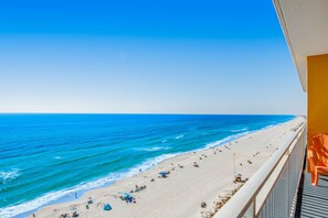 A beach view from a balcony with a clear sky, a sandy beach, and a few umbrellas. - Ocean and breachfront condo with pool, gym, hot tub - walk to the beach (Panama City Beach)
