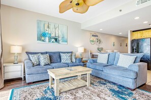 A living room with two sofas, a coffee table, and a painting on the wall. - Ocean and breachfront condo with pool, gym, hot tub - walk to the beach (Panama City Beach)
