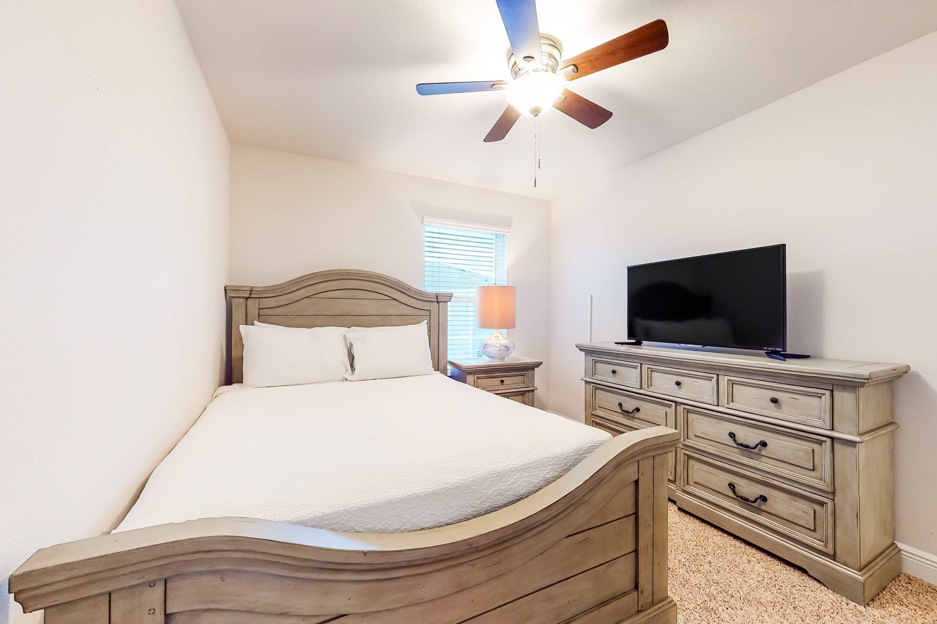 A bedroom with a bed, a dresser, a television, and a ceiling fan.