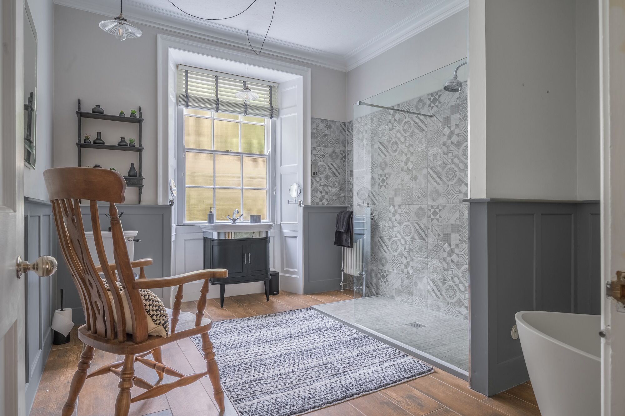 A bathroom with a shower, a sink, a chair, and a window with blinds.