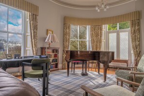 A spacious room with a grand piano, a comfortable sofa, a reading chair, and a bookshelf.
