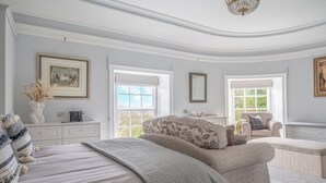 A bedroom with a large bed, a chaise lounge, a desk, and a chair.