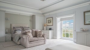 A bedroom with a large window, a bed, a sofa, and a dresser.