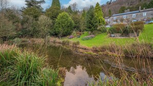 A serene landscape with a pond, lush greenery, and a stone building with a sloped roof.