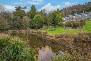 A serene landscape with a pond, lush greenery, and a stone building with a sloped roof.
