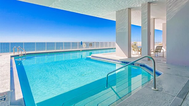En swimmingpool med kristallklart blått vatten, en metallstege och utsikt över havet.