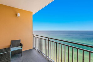 Ein Balkon mit Korbstuhl und kleinem Tisch, mit Blick auf das klare, blaue Meer.