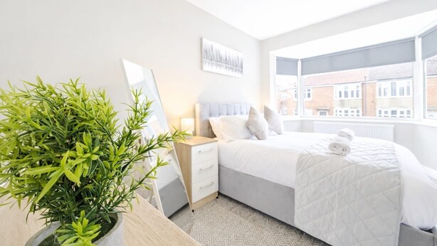 A hotel room with a bed, a bedside table, a mirror, a potted plant, and a window with a view of buildings. - 2 Bed Flat, Newcastle, 5 min to City, Free parking - Pass the Keys (Newcastle)