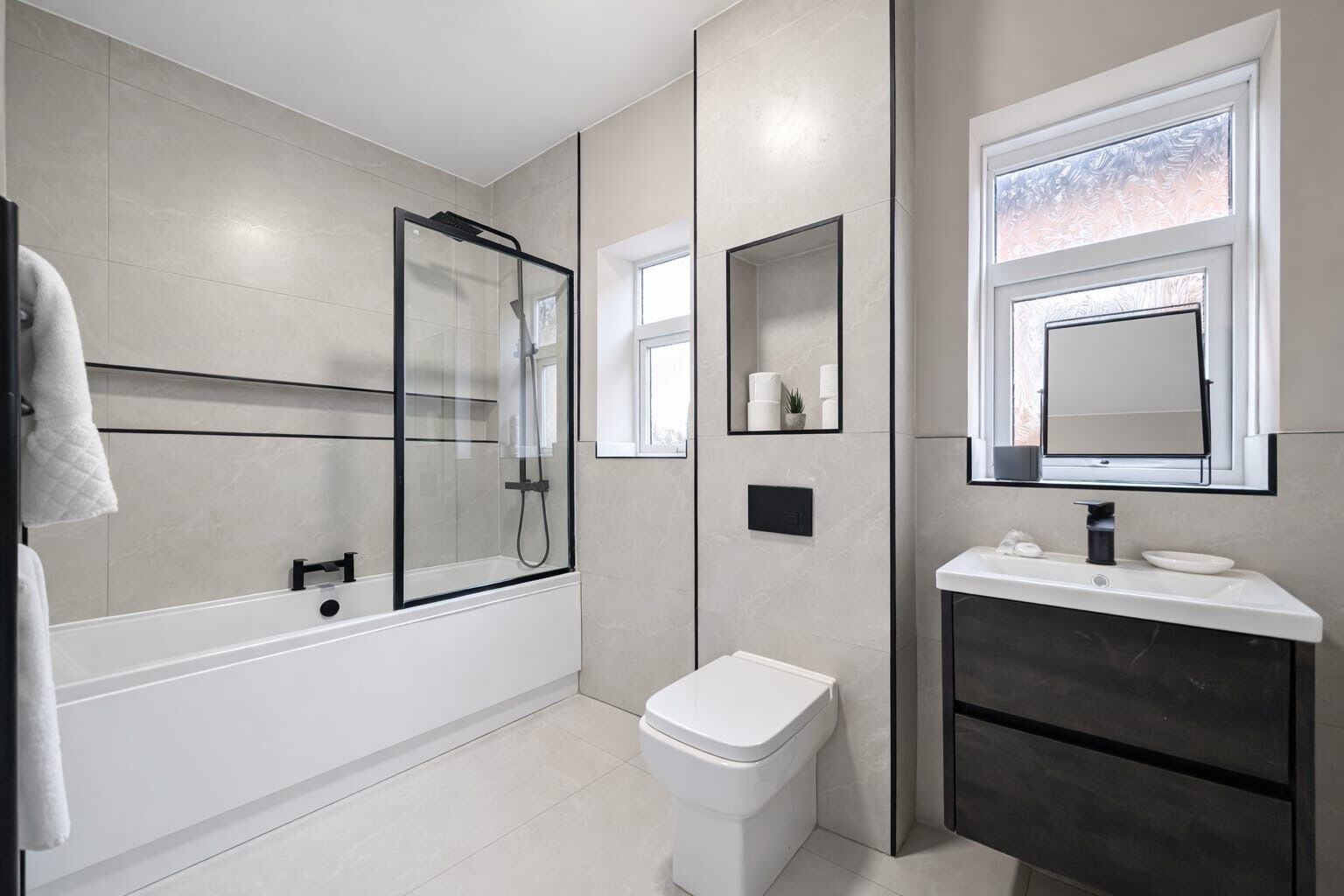 A modern bathroom with a glass-enclosed shower, a toilet, a sink with a mirror, and a window.