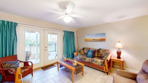 Ein Wohnzimmer mit Sofa, Sesseln, Couchtisch, Deckenventilator, Lampe und einem Gemälde an der Wand.