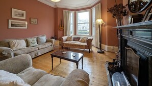 Ein traditionelles Wohnzimmer mit zwei Sofas, einem Couchtisch, einem Kamin und einem großen Fenster mit Vorhängen.
