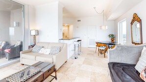 A modern living room with a sofa, a coffee table, and a dining area with a table and chairs. - Beautiful 28th-floor condo w/shared gym/Roman spa, hot tub, two shared pools (Panama City Beach)