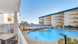 A swimming pool with a curved design, surrounded by a white fence and a building with multiple balconies. - First-floor condo with sauna, gym, pool, tennis & pickleball (Santa Rosa Beach)
