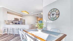 A modern kitchen with white cabinets, a central island, and a dining area with a wooden table and white chairs. - First-floor condo with sauna, gym, pool, tennis & pickleball (Santa Rosa Beach)
