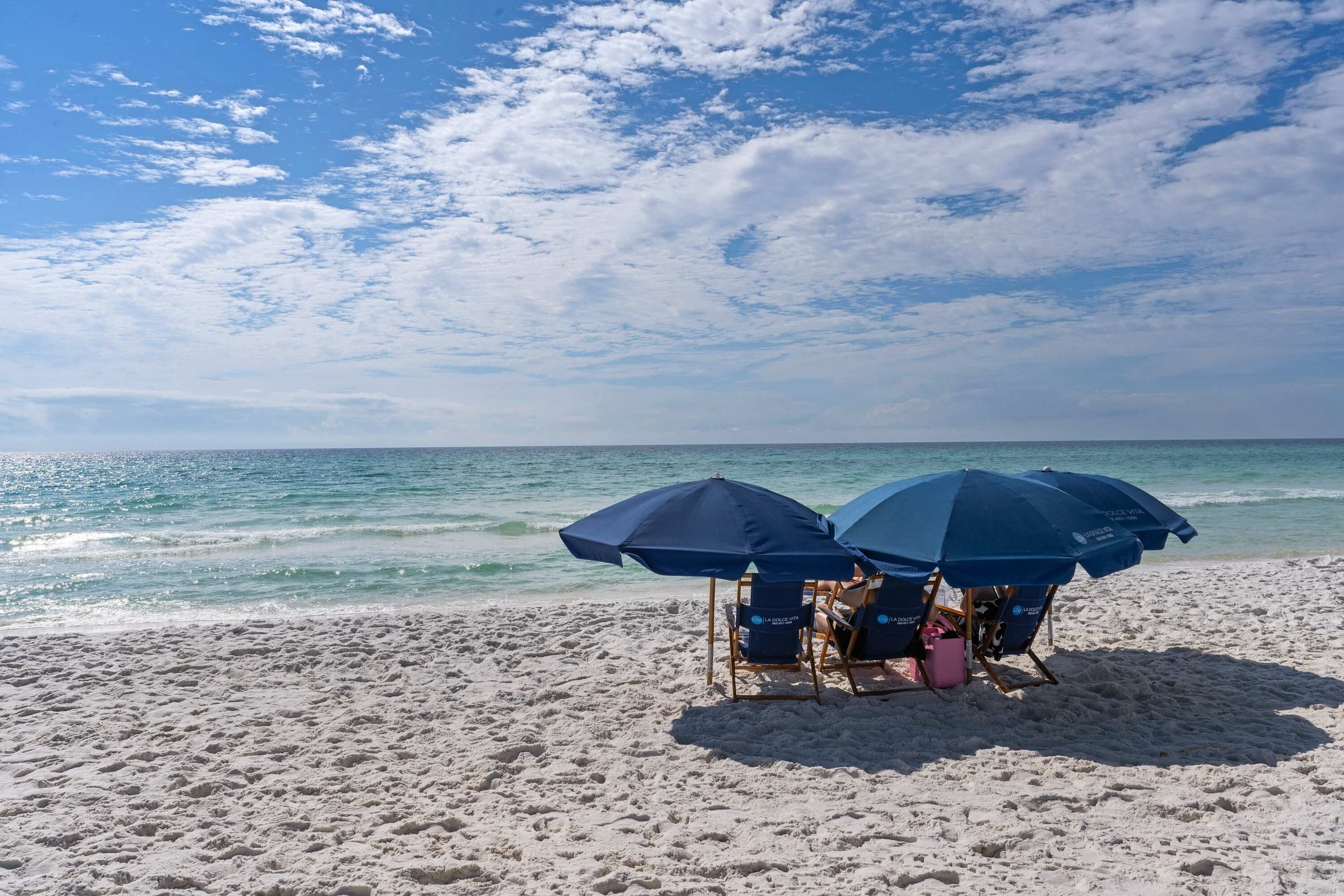 Una playa con dos sombrillas azules y sillas de playa.