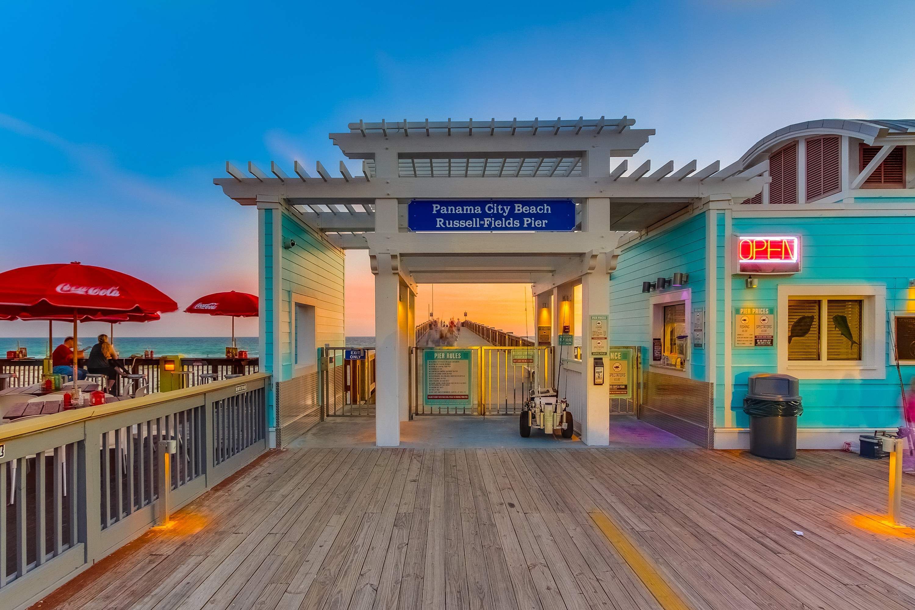 Een pieringang met een Coca-Cola parasol, een bord voor Panama City Beach en een neon 'OPEN' bord.