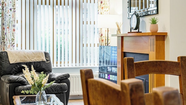 Ein Wohnzimmer mit einer Ledersofa, einem Holzstuhl, einem Glastisch und einem Kamin mit digitaler Anzeige.