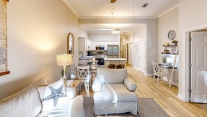 A spacious living room with a grey sofa, a starfish pillow, a ceiling fan, and a dining area with a table and chairs. - 4th-floor condo near the beach with balcony, outdoor pool, elevator, laundry, & AC (Santa Rosa Beach)