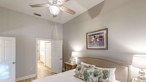 A bedroom with a bed, a ceiling fan, a nightstand with a lamp, and a framed picture on the wall. - 4th-floor condo near the beach with balcony, outdoor pool, elevator, laundry, & AC (Santa Rosa Beach)