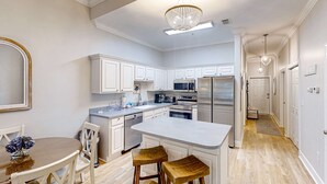 A modern kitchen with white cabinetry, a central island with stools, and a chandelier. - 4th-floor condo near the beach with balcony, outdoor pool, elevator, laundry, & AC (Santa Rosa Beach)