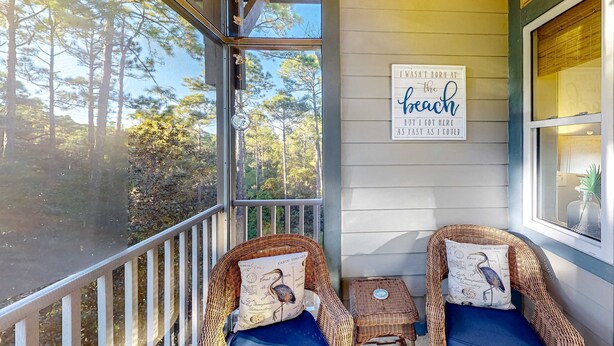A covered porch with wicker chairs, a small table, and a sign on the wall. - 4th-floor condo near the beach with balcony, outdoor pool, elevator, laundry, & AC (Santa Rosa Beach)