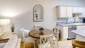 A compact kitchen with white cabinets, a round dining table with chairs, and a small island with a sink. - 4th-floor condo near the beach with balcony, outdoor pool, elevator, laundry, & AC (Santa Rosa Beach)