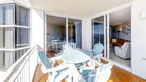 A balcony with a table and chairs, a sliding glass door leading to an interior space with a sofa and a lamp. - Coastal condo steps to beach with pools, hot tub, gym & amazing views (Perdido Key)