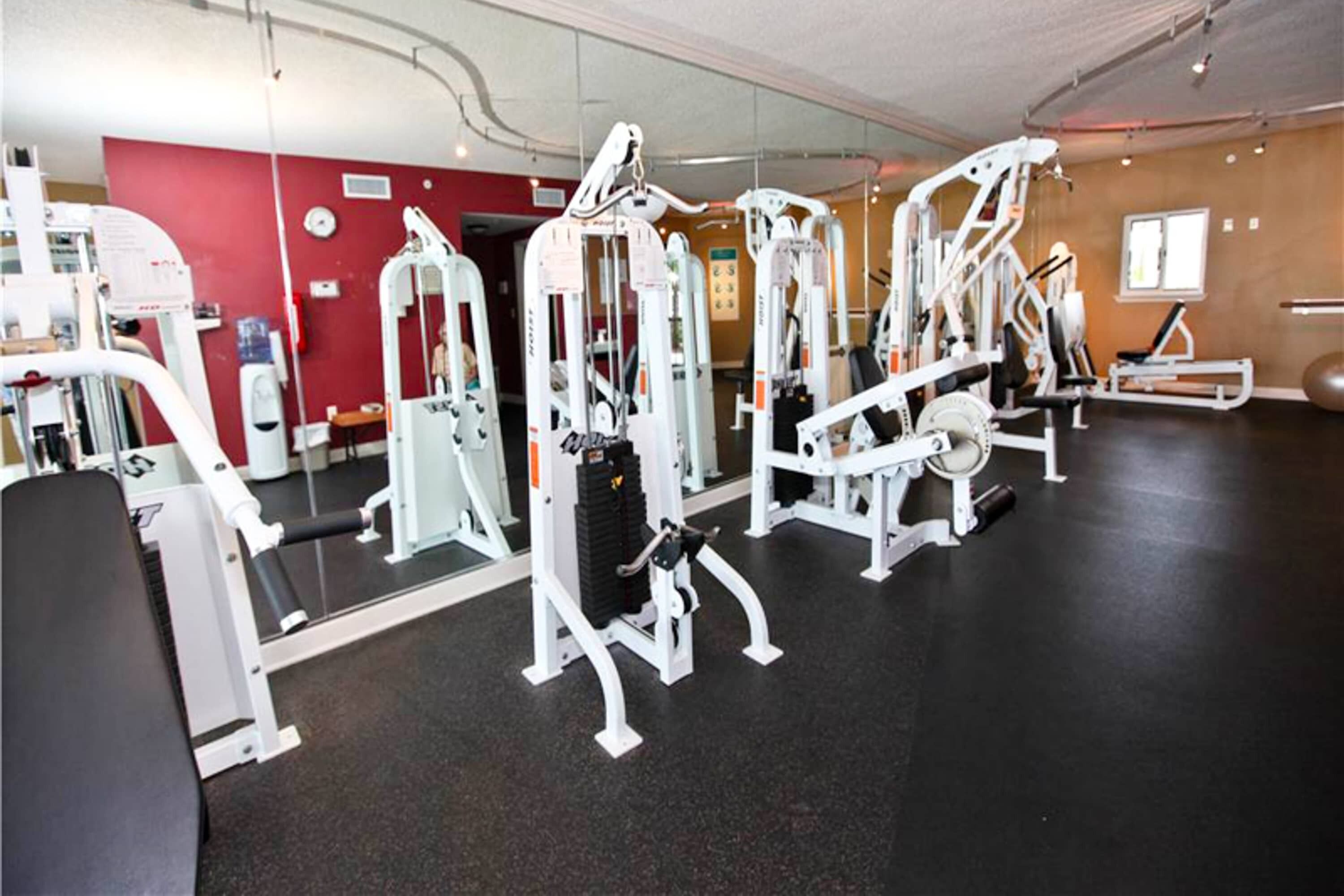 A gym with various exercise machines, a mirror, and a red wall.