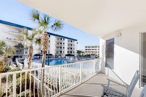A balcony with a pool, palm trees, and a view of a multi-story building with balconies. - Condo with 2 stunning pools, hot tub, gym, partial Gulf view & pickleball (Santa Rosa Beach)