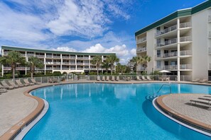 A swimming pool surrounded by a multi-story building with balconies and palm trees. - Condo with 2 stunning pools, hot tub, gym, partial Gulf view & pickleball (Santa Rosa Beach)