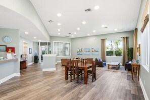 A spacious living area with a dining table, chairs, and a sofa. There is a kitchen area with a refrigerator and a water dispenser. - Condo with 2 stunning pools, hot tub, gym, partial Gulf view & pickleball (Santa Rosa Beach)