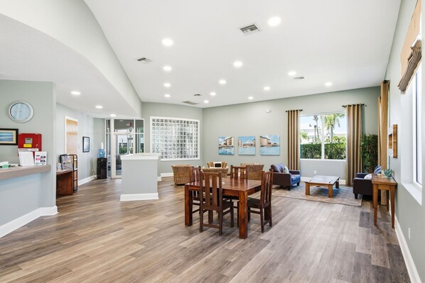 A spacious living area with a dining table, chairs, and a sofa. There is a kitchen area with a refrigerator and a water dispenser. - Condo with 2 stunning pools, hot tub, gym, partial Gulf view & pickleball (Santa Rosa Beach)