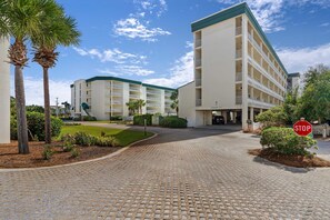 A hotel with a paved entrance, palm trees, and a stop sign. - Condo with 2 stunning pools, hot tub, gym, partial Gulf view & pickleball (Santa Rosa Beach)