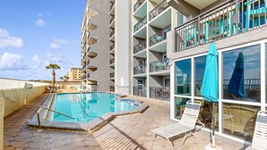 Une piscine avec un revêtement de sol en carrelage, des chaises longues et un balcon doté de balustrades.