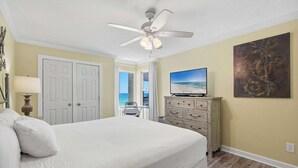 Une chambre à coucher avec un lit, un ventilateur de plafond, une commode, un téléviseur et un tableau.