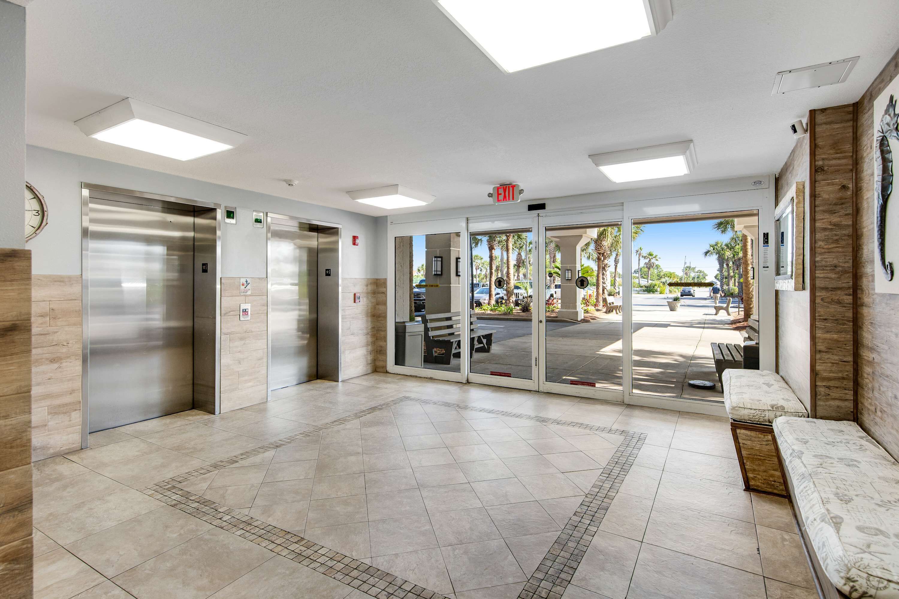 A lobby with elevators, a bench, and a view of the outside.